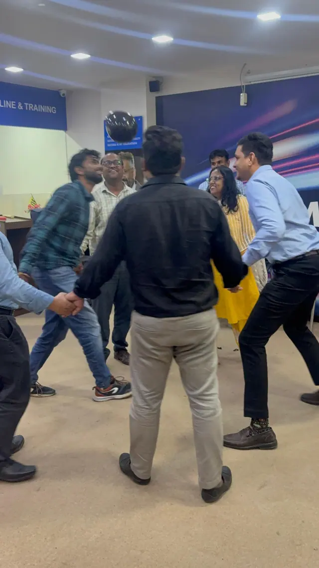 Colleagues holding hands in a circle keep a black balloon in the air.