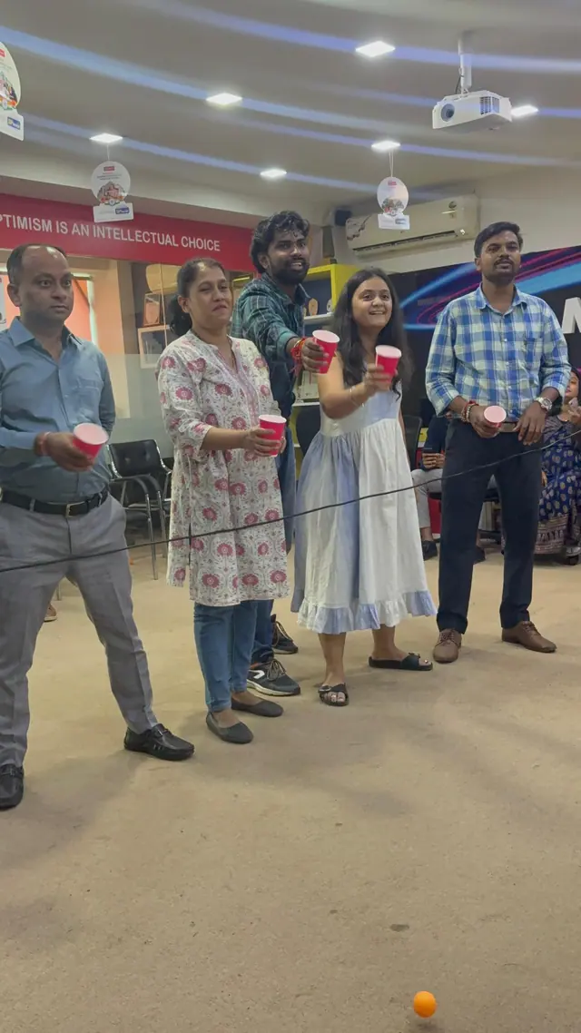 Five colleagues stand in a line holding red cups, ready to start a relay game.